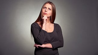 Mladá žena se zamyšleným výrazem vzhlížící vzhůru s rukou u brady